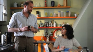 Ein Mann und eine Frau befinden sich in der Küche, beide haben eine Kaffeetasse in den Händen.