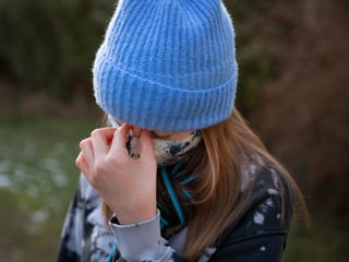 Teenager-Mädchen mit Mütze hält sich die Hand an die Nasenwurzel