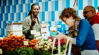 Marktstand mit Verkäufer und einer bunten Auslage von frischem Gemüse.