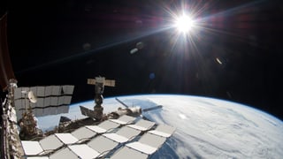 ISS, im Hintergrund scheint die Sonne auf die Erde.