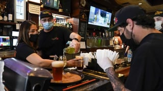 Personen mit Masken bereiten an einern Bar Drinks vor.