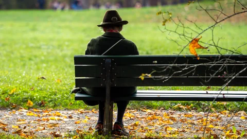 Person mit Hut sitzt auf einer Bank im Park.