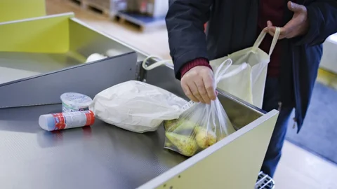 Jemand packt an einer Kasse Lebensmittel in einen Beutel.