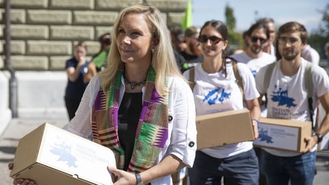 Zwei Frauen und ein Mann tragen Kartonboxen mit Unterschriftspapieren.