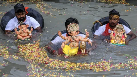 Drei Männer mit Ganesha-Statuen im Wasser.