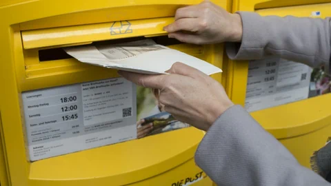 Eine Person wirft ein Stimmkuvert in einen Briefkasten.