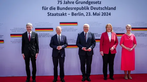 Drei dunkel gekleidete Männer und zwei Frauen. Die eine Frau trägt einen roten Rock und die andere eine rote Jacke