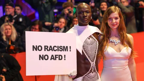 2 Personen am roten Teppich mit Protestplakat