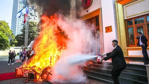 Mann löscht Feuer vor einem Gebäude mit Feuerlöscher.