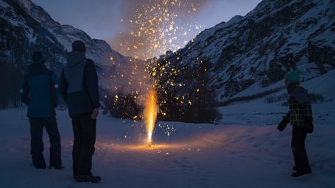 Menschen stehen im Schnee um einen Feuerwerkskörper herum