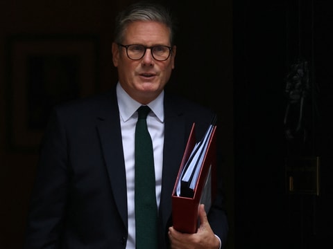 Keir Starmer mit Brille und Anzug hält Ordner.