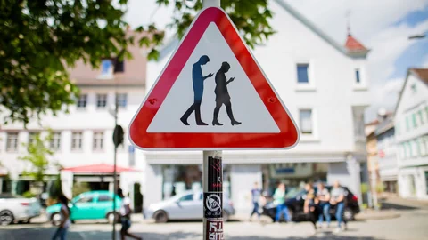 Warnschild mit zwei Figuren, die auf ihr Handy schauen.