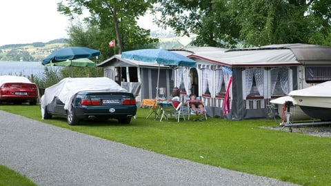 Wohnwagen mit Vorzelten und davor parkierte Autos auf einem Campingplatz.