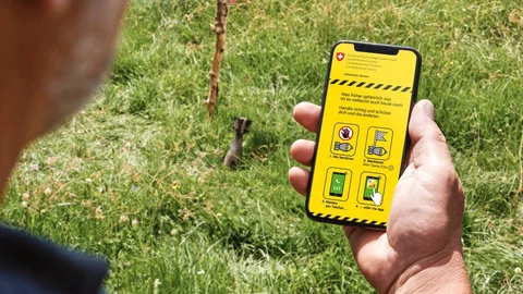 Person betätigt Warn-App auf Smartphone vor Munition im Gras.