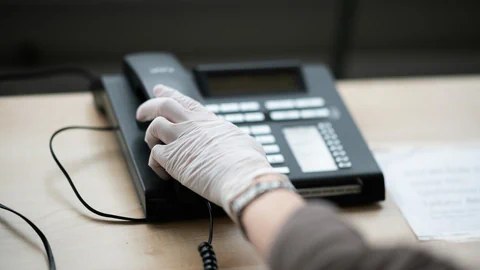 Frauenhand mit Handschuh greift zum Telefonhörer.