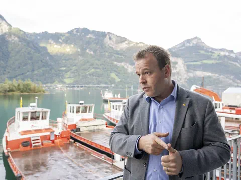 Mann steht vor Booten und Bergen am Wasser.