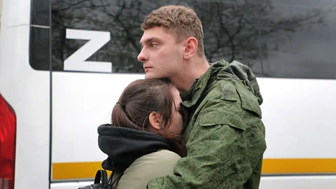 Soldat in Uniform umarmt Frau vor einem Bus.