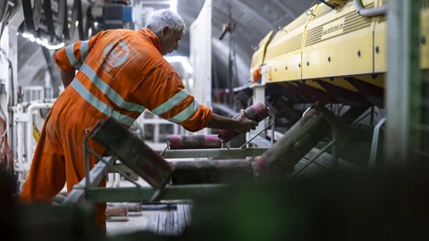 Arbeiter in orangefarbener Schutzkleidung bei Wartung von Maschinen.