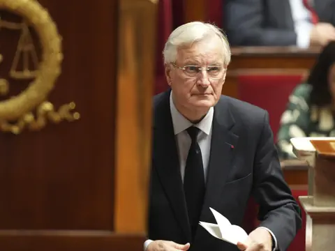 Michel Barnier im Anzug hält Dokument in Konferenzraum.