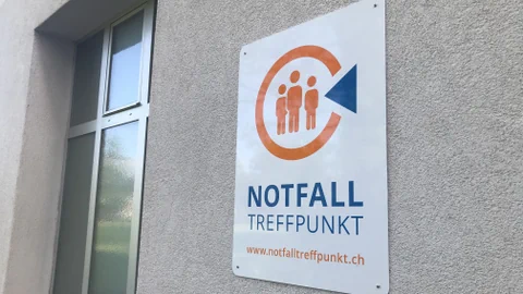 Das Schild mit dem Logo der Notfalltreffpunkte hängt an einer hauswand.