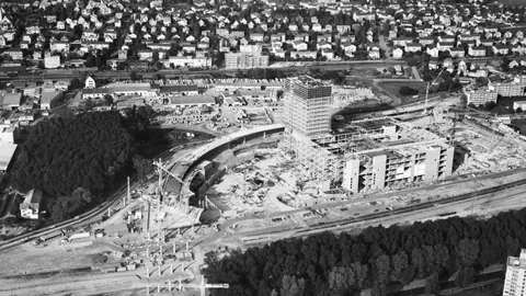 Eine Schwarz-Weiss-Aufnahme einer Baustelle zeigt ein grosses Gebäude neben einer Autobahn.