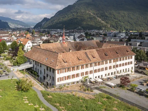 Luftaufnahme eines historischen Gebäudes in einer Stadtlandschaft mit Bergen.