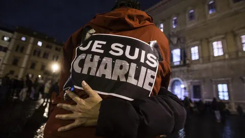 Menschen umarmen sich bei Nacht mit 'Je Suis Charlie'-Schild.