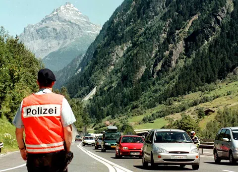 Polizist mit roter Warnweste und Aufschrift Polizei von hinten neben einer Autokolonne