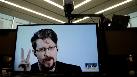 Bildschirm mit Videokonferenz, Edward Snowden zeigt Friedenzeichen.