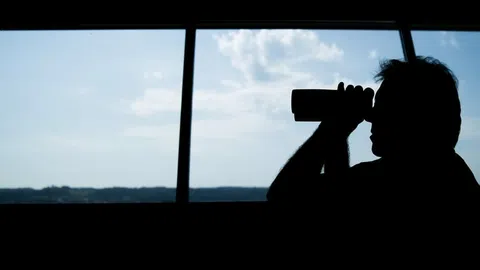 Mann mit Fernglas vor grossem Fenster.