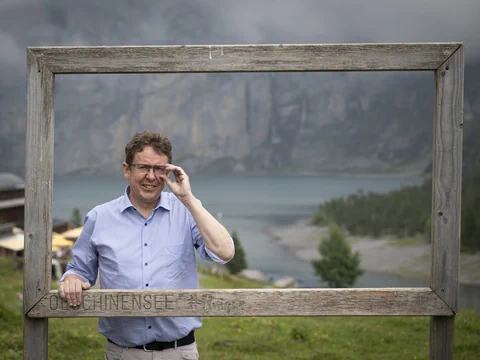 Mann steht hinter Holzbilderrahmen mit See im Hintergrund.