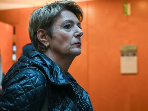 Frau mit kurzem Haar und schwarzer Jacke vor orangefarbener Wand.