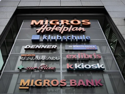 Verschiedene Logos an einer Gebäudefassade, darunter Migros, Hotelplan, Migros Klubschule, Zur Rose.