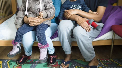 Eltern mit zwei Kindern sitzen gemeinsam auf einem Bett.