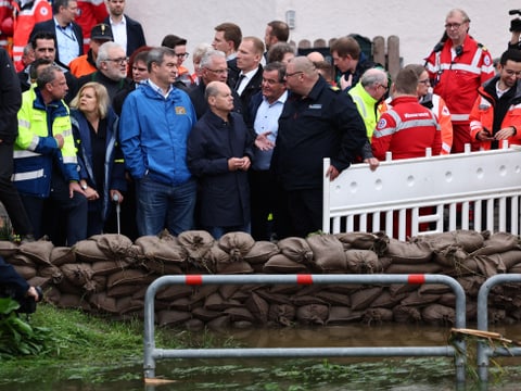 Eine Gruppe von Menschen, darunter Rettungskräfte, steht hinter Sandsäcken angesichts einer Überschwemmung.