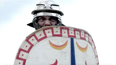 Ein als Römer-Soldat verkleideter Mann duckt sich hinter seinem Schild