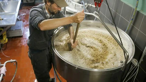 Ein Bierbrauer rührt in einem Kessel.