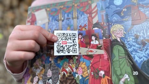 Adventskalender nah und das erste Türchen von einer Kinderhand geöffnet. Man sieht einen QR Code mit SRF Kids Signet.