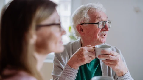 Eine Frau (verschwommen, links) und ein älterer Mann trinken zusammen Kaffee.