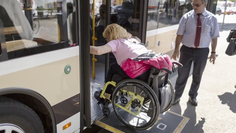 Eine Rollstuhlfahrerin fährt in einen Bus, der Chauffeur steht daneben.