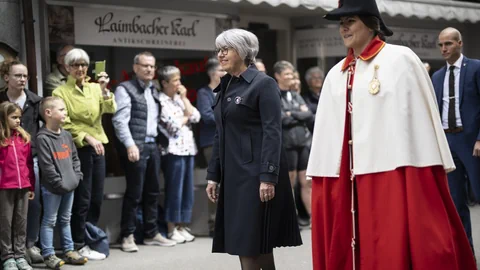 Zwei Frauen in formeller Kleidung, eine in Rot-Weiss, die andere in Schwarz, gehen auf einer Strasse.