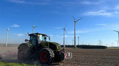 Traktor auf Feld, im Hintergrund Windräder