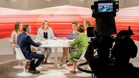 Man sieht die beteiligten Personen am Club im Fernsehstudio sitzen.