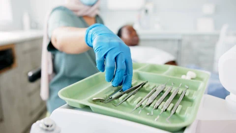 Zahnarzt mit blauen Handschuhen, der Dentalinstrumente aus einem Tablett nimmt.