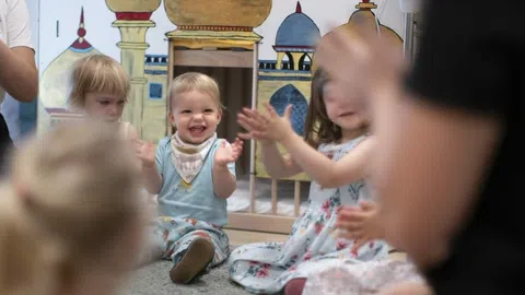 Kleine Kinder sitzen im Kreis in einer Kita, im Vordergrund Betreuer