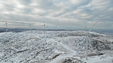 Windpark auf schneebedecktem Hügel unter bewölktem Himmel.