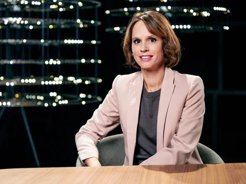 Frau in rosa Blazer sitzt an einem Tisch.