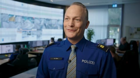 Lächelnder Polizeibeamter in Uniform in einem Überwachungsraum.