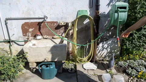 Brunnen, Giesskanne und Wasserschlauch in einem Garten.