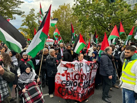 Menschenmenge bei einer Demonstration mit palästinensischen Flaggen und Transparent.